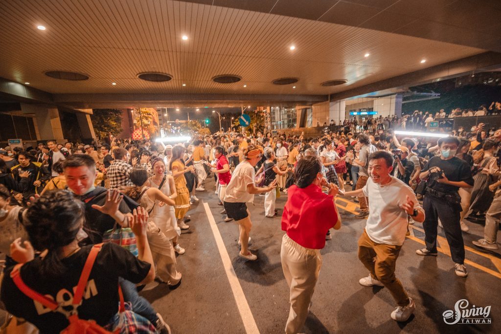 戶外大型活動現場，上百人在馬路上一起跳搖擺舞